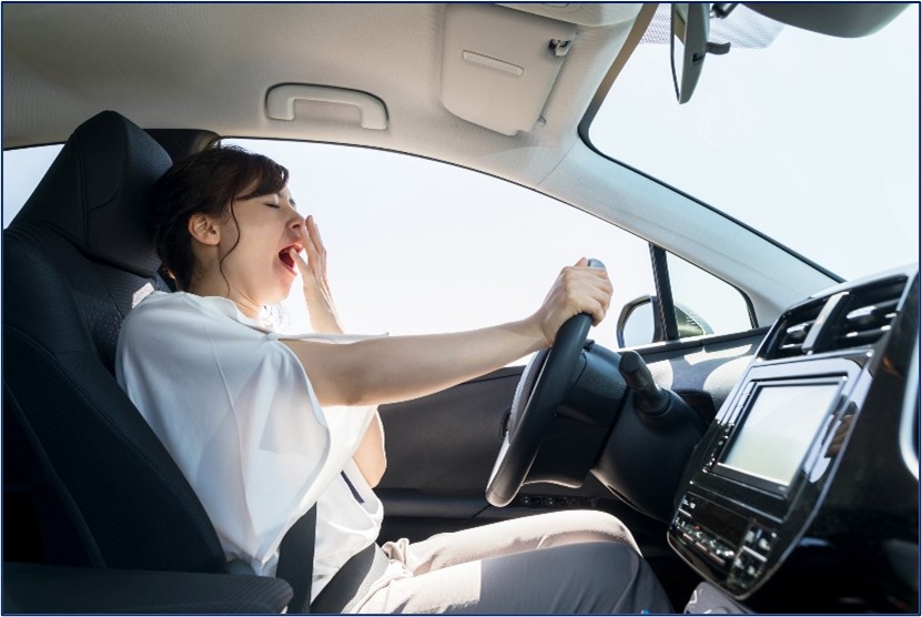A woman yawning while behind the wheel of a vehicle.