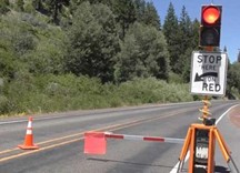 An Automated Flagger Assistance Device deployed along a two lane road, with the signal 'red' and the flagger arm extended down. 