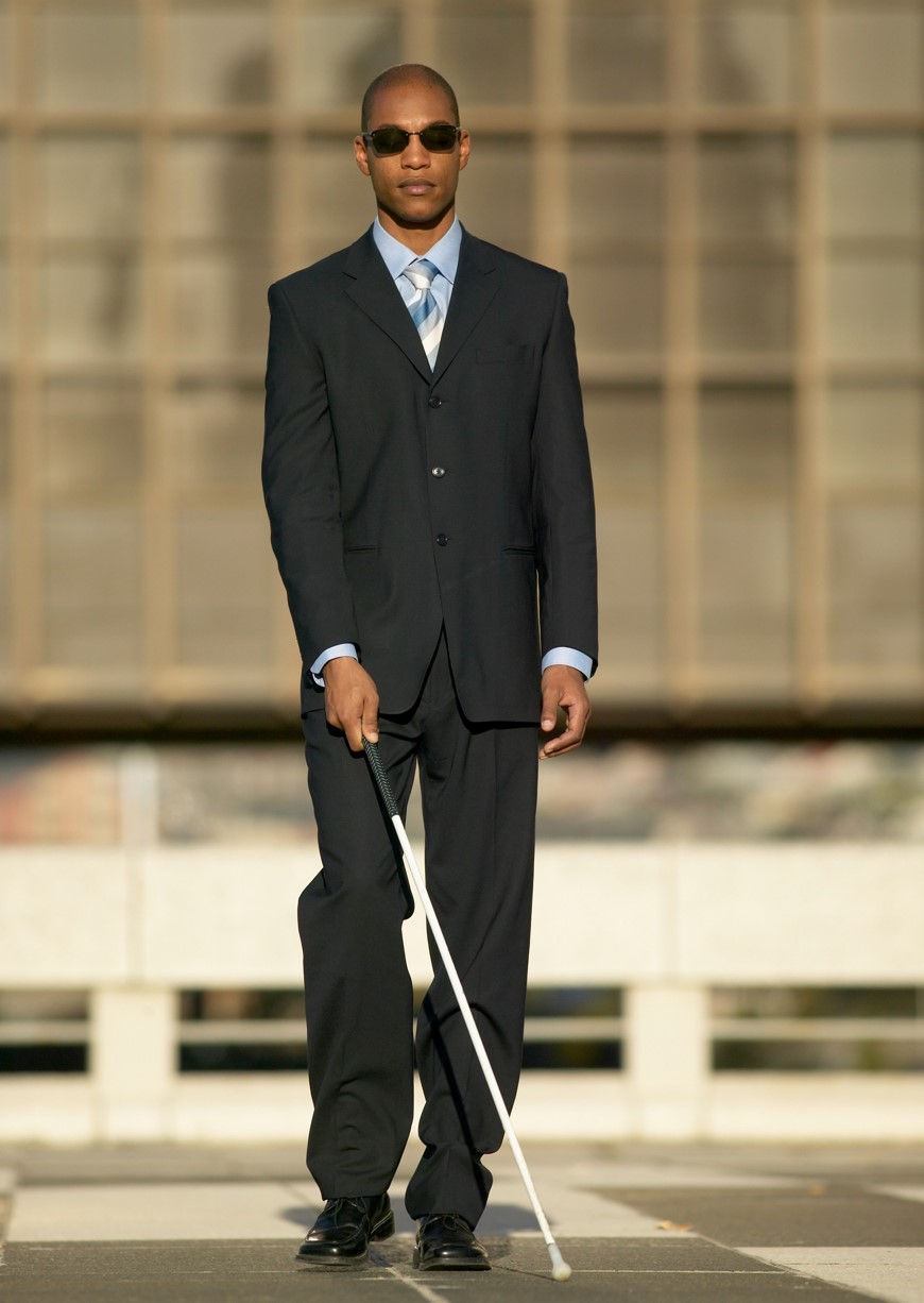 A visually impaired man walking outside with the assistance of a white cane.