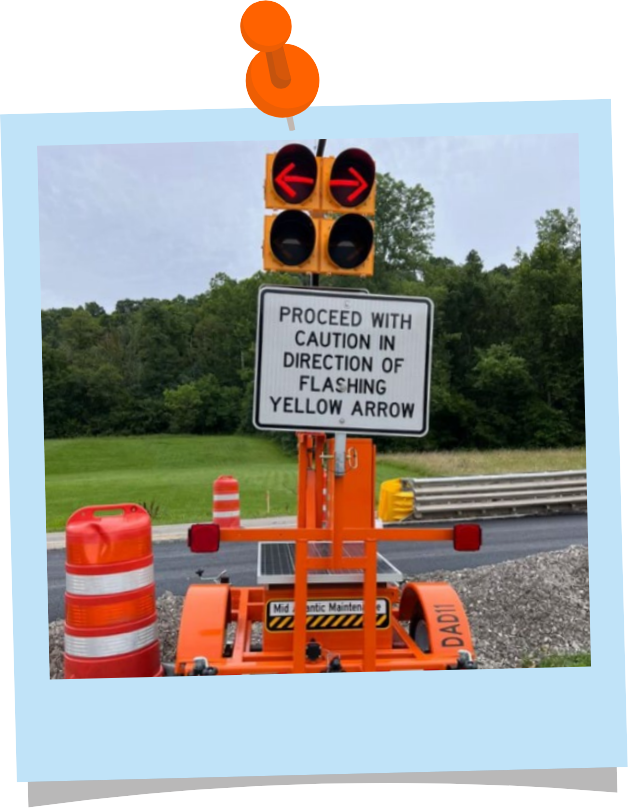 An orange driveway assistance device. A four circle signal sits at the top of the device. There are two red arrows pointing left and right in the top two circles. Below the signal is a sign that reads "proceed with caution in direction of flashing yellow arrows."