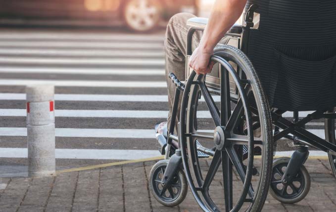 A person in a wheelchair is waiting to cross an intersection with a vehicle shown in the distance.