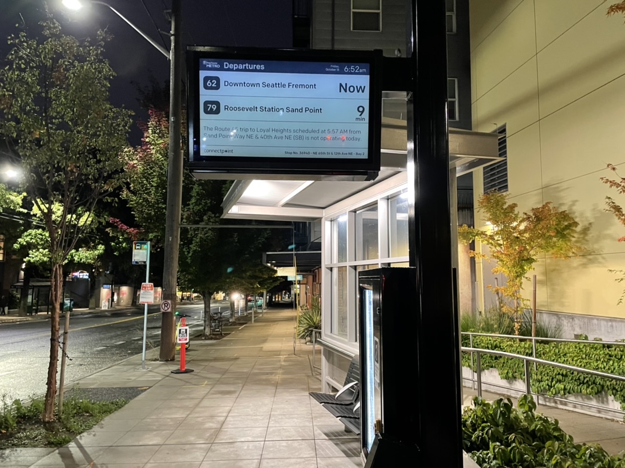 A digital transit signed mounted on a large pole/mast arm along a sidewalk.