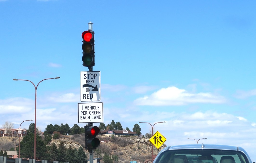 Picture of a car waiting at a ramp meter, which is currently displaying a red signal