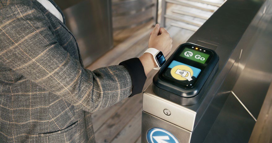 A man holding up a smart watch to a turnstile to pay.