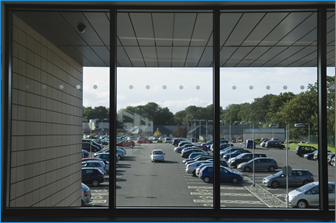 View outside of a window of an office parking lot, with a car looking for parking