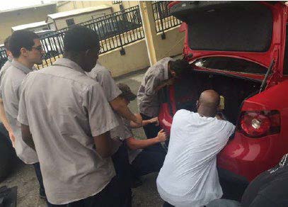 Community college students installing connected vehicle equipment in the trunk of a pilot participant's vehicle.