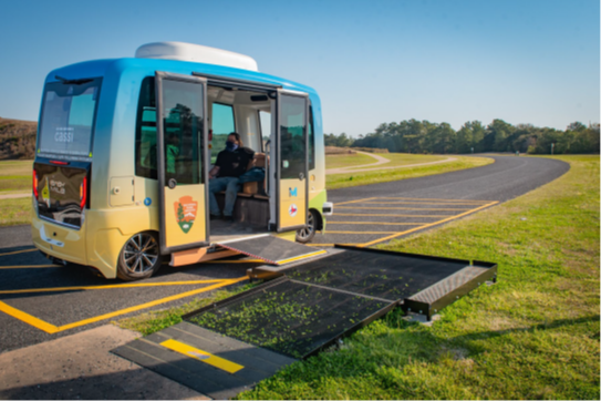 A parked automated shuttle with a passenger onboard and the doors open with the ramp deployed.
