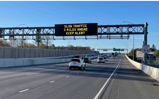 Image of cars on an interstate traveling under a dynamic message sign displaying a warning of slow traffic ahead