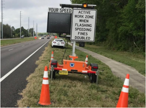 Portable work zone awareness device on the side of a two lane road. Device has two signs: the left sign shows the drivers speed in the work zone and the right sign displays the message "active work zone when flashing speeding fines doubled."