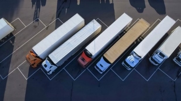 A parking lot with six tractor trailers parked next to each other.