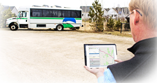 A man standing in front of a white bus holding his ipad. The ipad is displaying a map and other information to help with trip planning. 