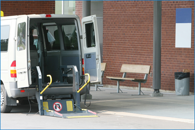 A wheelchair accessible vehicle parked along a curb with its wheelchair lift deployed. 