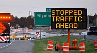 Image of a sign displaying the words "Stopped Traffic Ahead," with construction work happening behind the sign