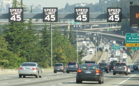 Image of vehicles on an interstate traveling under a series of variable speed limit signs mounted overhead, displaying that the speed limit is 45 miles per hour