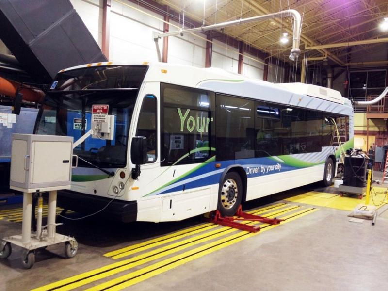 A transit bus parked inside a transit station garage with it's front wheel in a lift