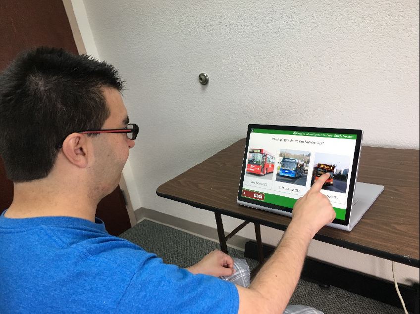 Image of a study participant using a touch screen notebook computer to engage in a software assessment application to determine his ability to identify buses by their numbers.