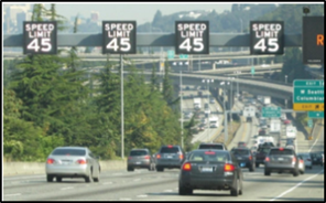 A busy highway with variable speed limit signs displayed over the driving vehicles.